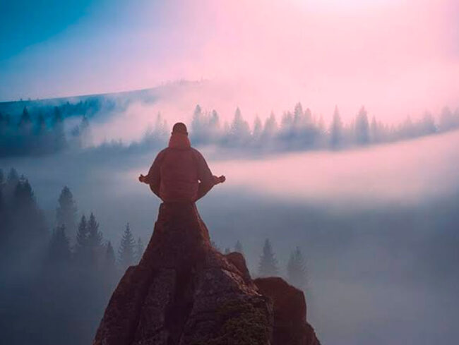 o que é uma emoção negativa? iogue meditando no topo da montanha
