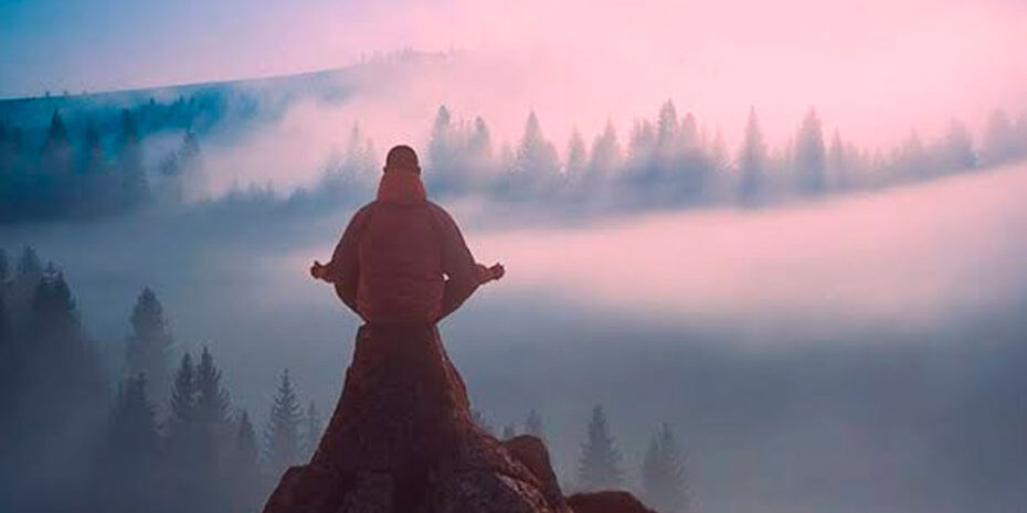 o que é uma emoção negativa? iogue meditando no topo da montanha